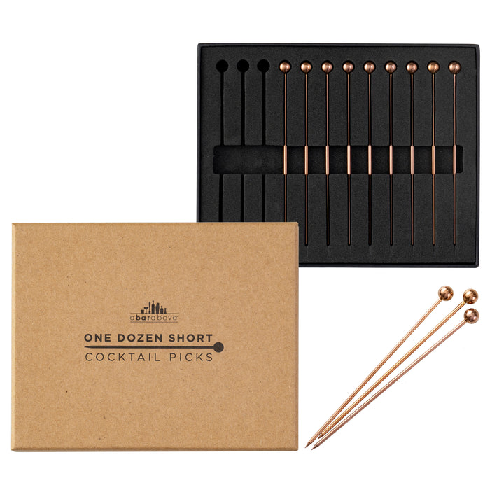 A dozen antique copper cocktail picks with spherical tops, displayed in their packaging and three loose.