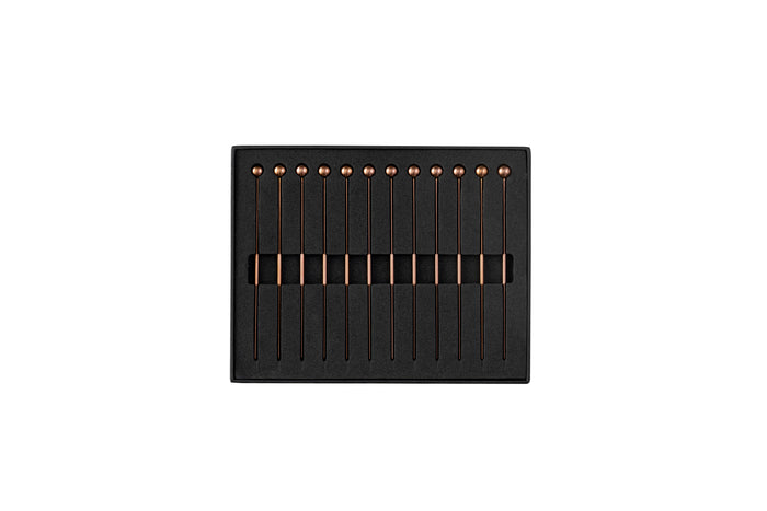 Twelve antique copper cocktail picks, each with a spherical top, neatly arranged in a black foam-lined box.