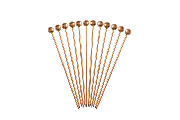 Set of eleven antique copper cocktail picks fanned out on a white background.