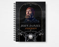 Beyond the Open Road memorial guest book front cover, black spiral-bound design with a bearded man in a rust-colored beanie, copper arch, white and copper lettering, motorcycle handlebars and headlight, Standard size.