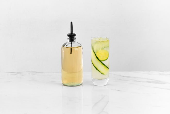 Black pour spout inserted into a glass bottle, reflected on a glossy white marble surface.