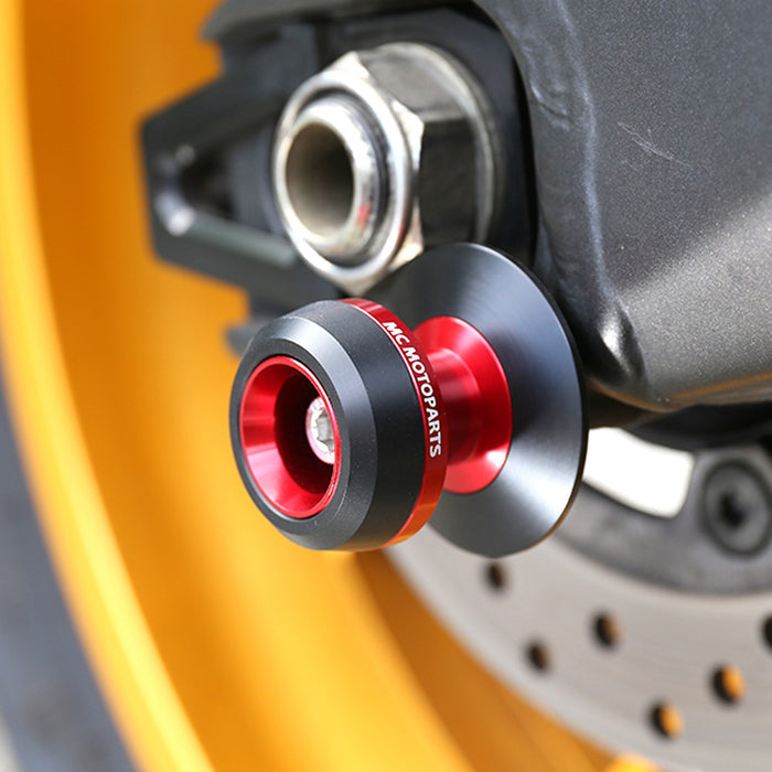Red MC Motoparts swingarm spools for Aprilia Dorsoduro 750, 900, 1200 models, installed on motorcycle swingarm.