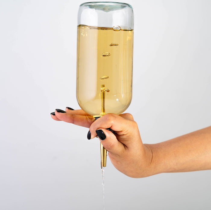 Gold pour spout held by a hand, attached to an inverted bottle pouring clear liquid.