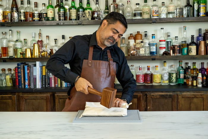 Bartender using a natural canvas Lewis bag and wooden mallet to crush ice.