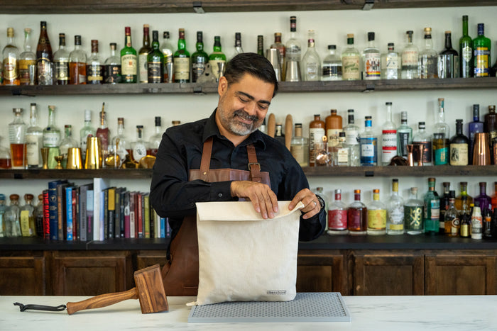 A man in a bar setting holds open a cream-colored Lewis bag, with a wooden mallet nearby.